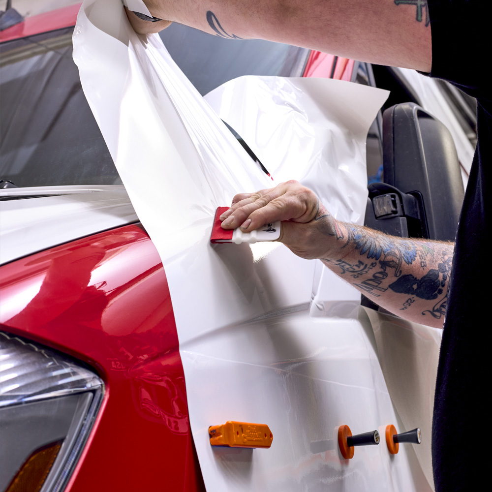 Car wrapping, mechanic with squeegee installs film